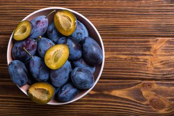 Fresh plums in bowl on wooden table . Fruit background