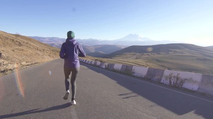 Young muslim woman in hijab running on mountain road,sun glare,rear view,slow mo