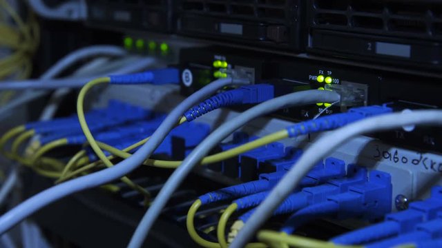From below closeup view of glowing indicators of server hardware in racks with blue cables
