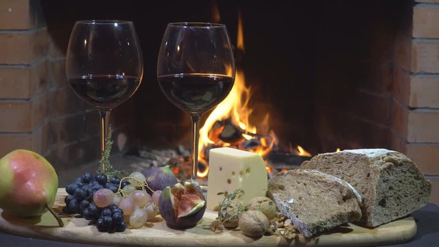 Two glasses of wine, cheese, bread and fruit on fire background, dolly shot