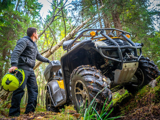 A man in an all-terrain vehicle. Forest. ATV. Leisure. A man goes on the road on the ATV. The traveler holds a helmet in his hands. Off-road.