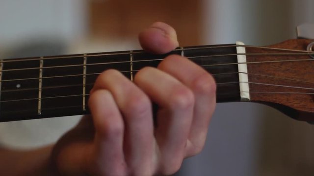 A close up of a young man is playing guitar, the camera pans left to show his strumming hand.