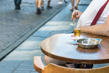 Fototapeta na wymiar A man with big belly sittiing outdoors in a bar with an arm on round wooden table drinking beer.