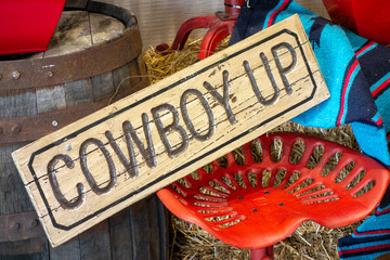 Western decor with Cowboy up sign and painted red vintage tractor seat - obrazy, fototapety, plakaty