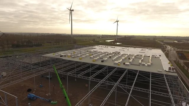 Flying with a drone over a construction site where a warehouse is being build.
