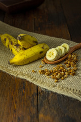 Some bananas and a banana sliced into a wooden spoon with cereal and honey