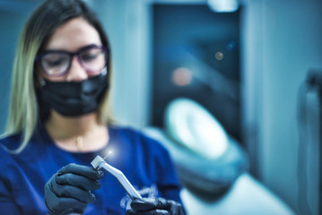 Selective focus Dentist in gloves holding in hand dental drill with flash The hand with drill is focused. female dentist with black surgical mask defocused . Blue cold tones Horizontal