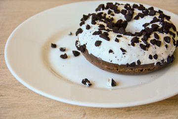 Delicious chocolate donut with white icing sprinkled with chocolate chips on a white plate