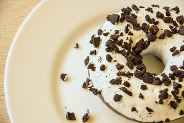 Delicious chocolate donut with white icing sprinkled with chocolate chips on a white plate