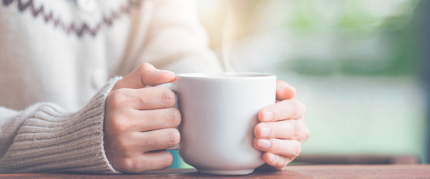 Woman hand in warm sweater holding a cup of coffee.Web banner.