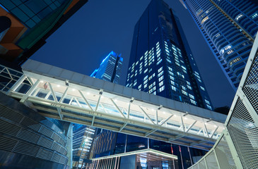 Fototapeta na wymiar Low angle view of walkway bridge and skyscraper office building , night scene