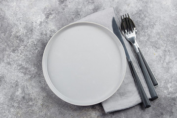 Empty ceramic grey plate and cutlery, knife, fork, spoon on gray stone concrete table background. Copy space. Menu Recipe Concept