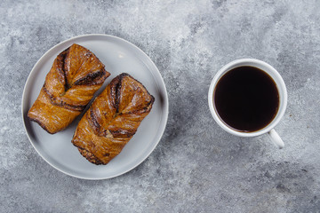 Fresh Pastry Bun and Cup of hot coffee on gray stone concrete table background. Top view, copy space. Breakfast Concept