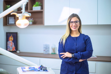 Portrait of woman dentist smiling in dental office dressed in blue medical uniform