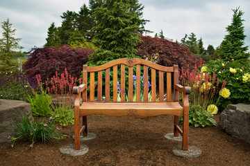 View of wooden bench in picturesque garden with blue sky and wispy white clouds