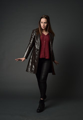 full length portrait of brunette girl wearing long leather coat and boots. standing pose  on grey...