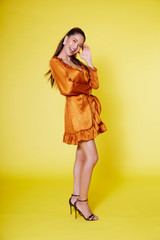 Young tan asian woman in orange dress acting face over yellow background 
