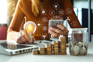 business woman hand holding lightbulb with using smartphone and calculator to calculate and money...