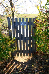 Holztür in einer Hecke mit der Aufschrift Durchgang auf eigene Gefahr