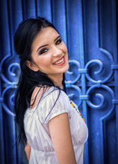 Beautiful brunette girl with big eyes and white dress, smiling over the shoulder next to a blue door