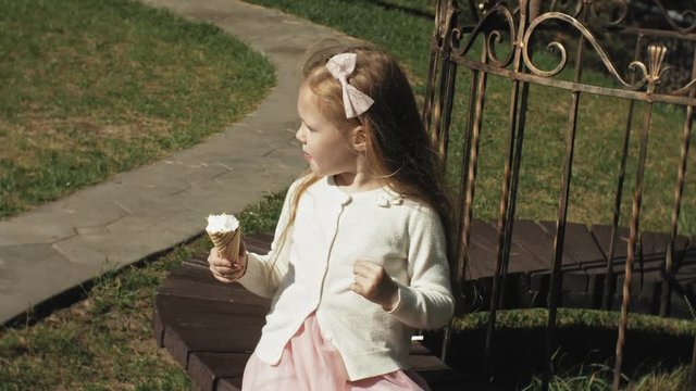 A cute girl is sitting in the park and eating ice cream
