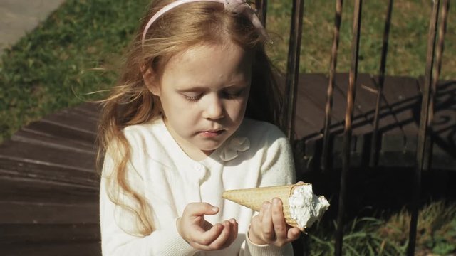 A cute girl is sitting in the park and eating ice cream