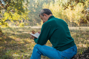 Alone sad senior man with a book on a nature, concept of loneliness 