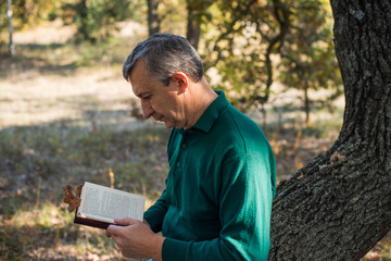 Alone sad senior man with a book on a nature, concept of loneliness 