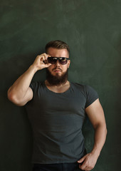 Obraz premium Bodybuilder in sunglasses portrait. Muscular man with a beard in a tight t-shirt straightens his glasses. Stylish and sporty.