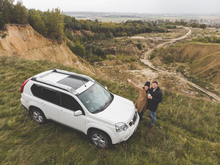 couple standing near suv car at the cliff with beautiful view from the top.