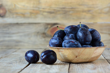Ripe blue plums with drops of water in a wooden bowl on a wooden background