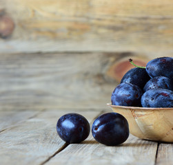 Fresh blue plums with drops of water in a wooden bowl on a wooden background