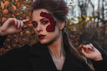 Beautiful young girl with applique red roses flowers on the face in nature autumn