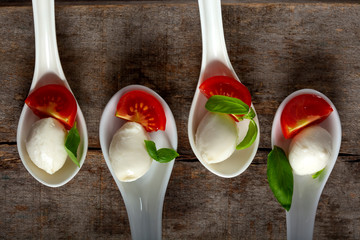 Spoons with mozzarella cheese balls, cherry tomato and basil on wooden background © Sebastian Studio