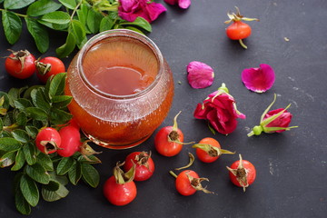 A jar of wild rose jam, next to a twig from the garden with berries and flowers