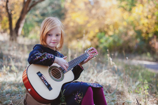 Girl playing guitar in the autumn forest