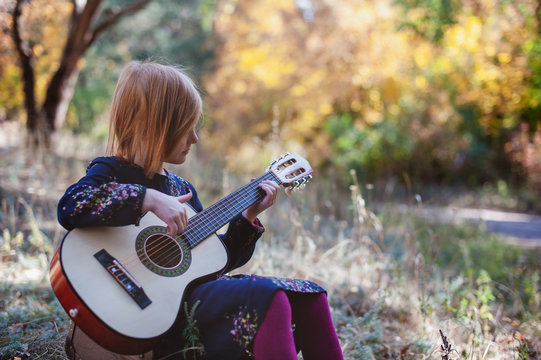 Girl playing guitar in the autumn forest