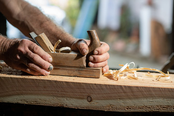 Handwerkerhände mit altem Holzhobel beim abhobeln eines Hozbalken - obrazy, fototapety, plakaty