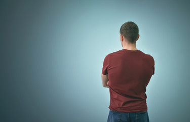 Young man in t-shirt is standing and is looking ahead with his arms crossed isolated on blue background.