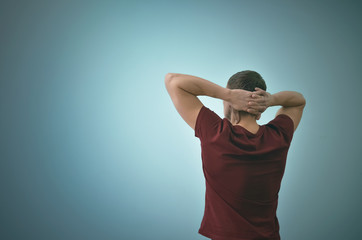 Thinking man is standing and is relaxing and is looking ahead by holding his hands behind his head.