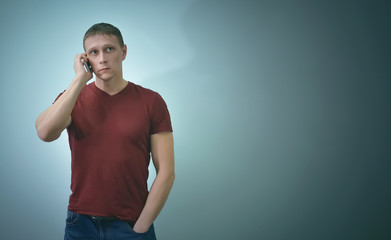 Young man is talking by mobile phone in his hands and looking up isolated on blue background with...