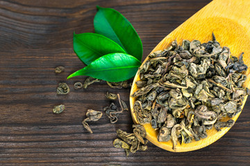 Spoon of dry tea with green tea leaves on wooden background