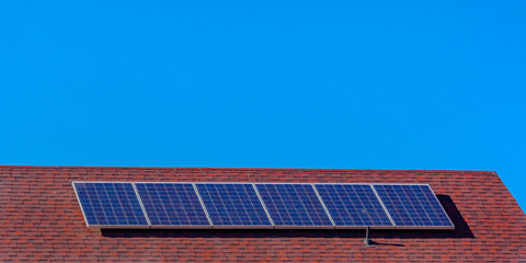 Fototapeta premium Solar panels on a red roof beneath clear blue sky