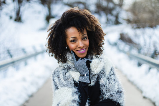 Cheerful Stylish Afro Hair Woman Portrait Under The Snow At Winter Mountain Road. Female Wearing Warm Clothes And Gloves.