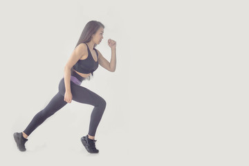 Side view full length portrait of a young fitness woman running isolated over gray background