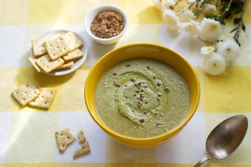 Vegetable soup with broccoli, served with crackers, linseed oil and seeds.