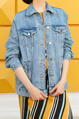 A stylish girl is dressed in a denim jacket and in a yellow skirt with an ornament stands straight. Street fashion.