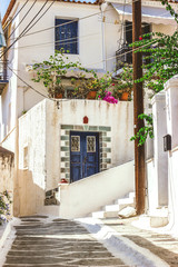 Narrow street in Neorio town on Poros island, Greece. Old white house with blue door and flowers