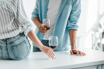 cropped image of couple with glasses of red wine in kitchen