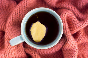 cup of coffee with an autumn leaf on a knitted rug close-up, top view